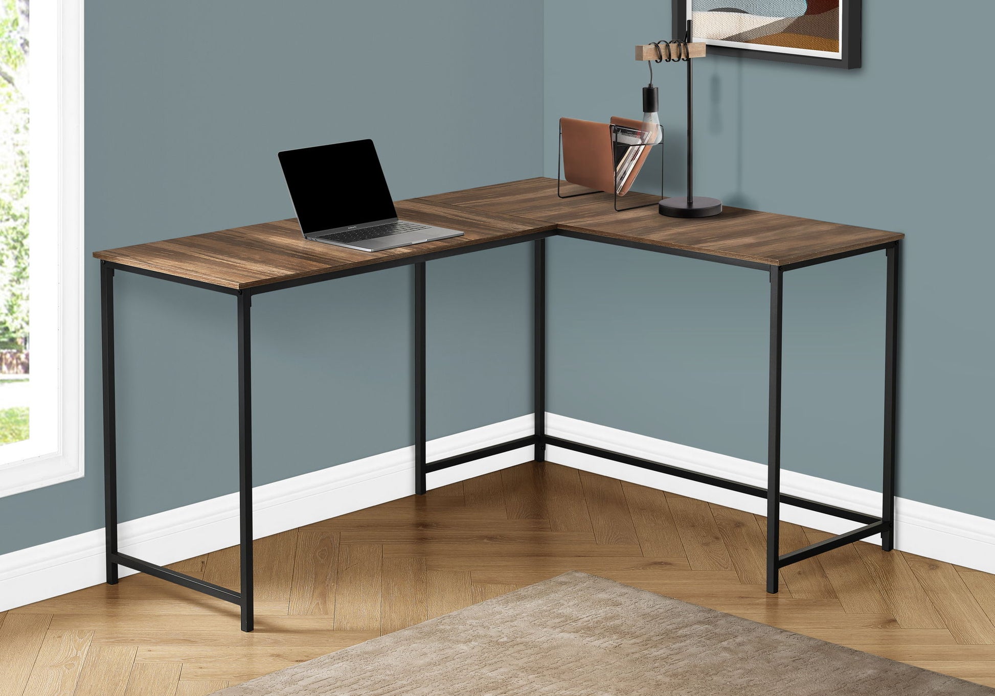 The Computer Desk Home Office, Corner, L Shape, Contemporary & Modern features a wood surface and black metal frame on a herringbone floor. On the desk are a laptop, lamp, and books. The room has blue-gray walls and a beige rug.