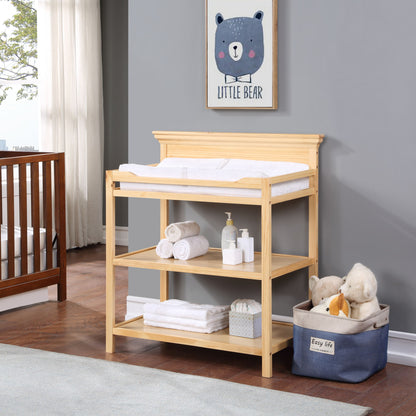 The Universal - Changing Table, topped with towels, baby supplies, and stuffed animals, stands in a nursery. Above it is a framed "Little Bear" picture, with a crib and window shown in the background.