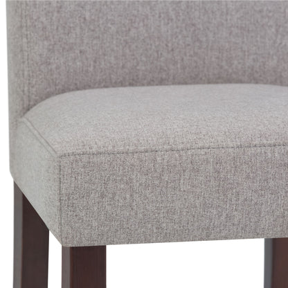 Close-up of the Acadian - Upholstered Parson Dining Chair seat, featuring light gray fabric, dark wooden legs, and a straight, partially visible back. Set of 2.