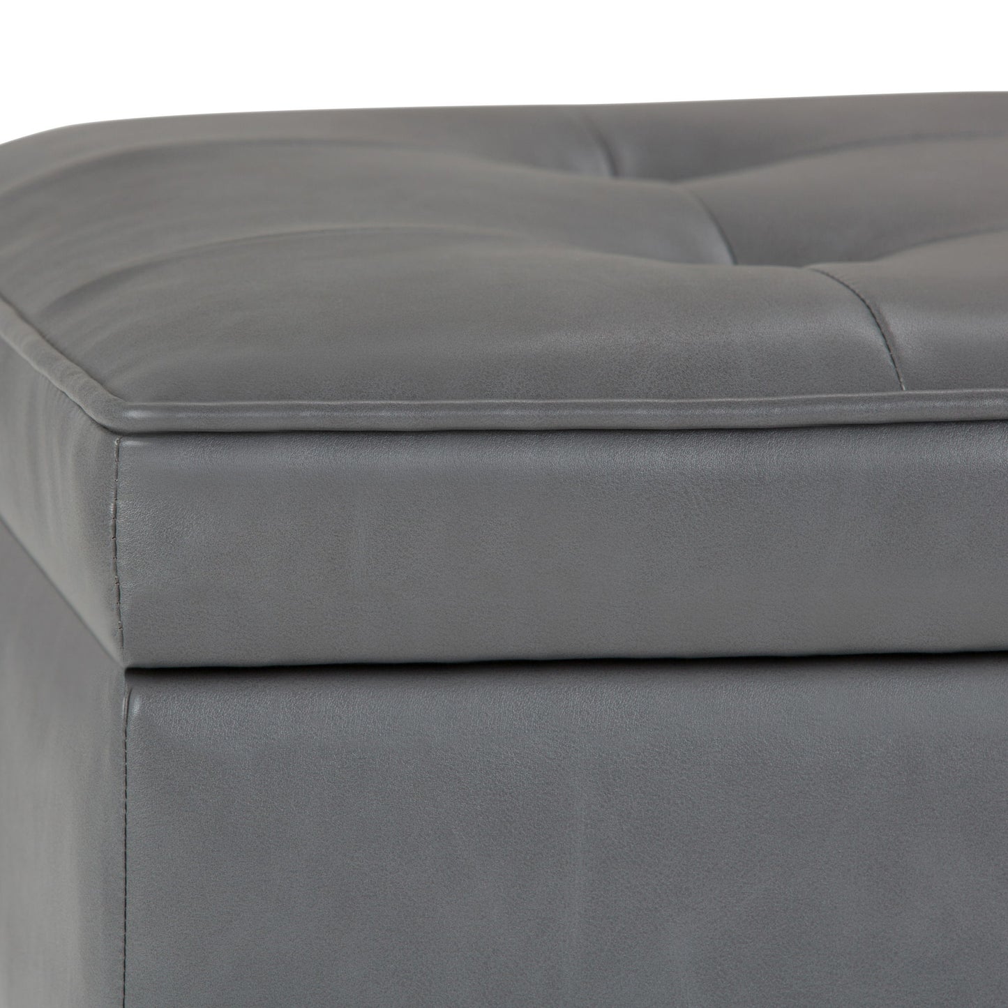 Close-up of the Cosmopolitan Storage Ottoman Bench with open bottom, showing gray tufted faux leather upholstery, visible stitching, padded corner, and part of the top cushion.