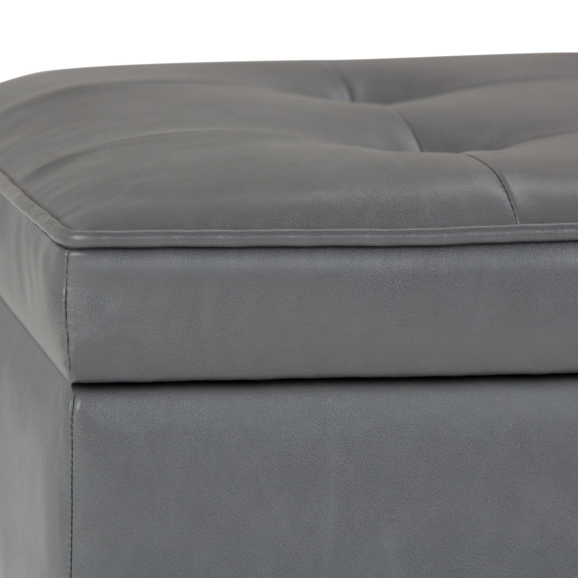 Close-up of the Cosmopolitan Storage Ottoman Bench with open bottom, showing gray tufted faux leather upholstery, visible stitching, padded corner, and part of the top cushion.