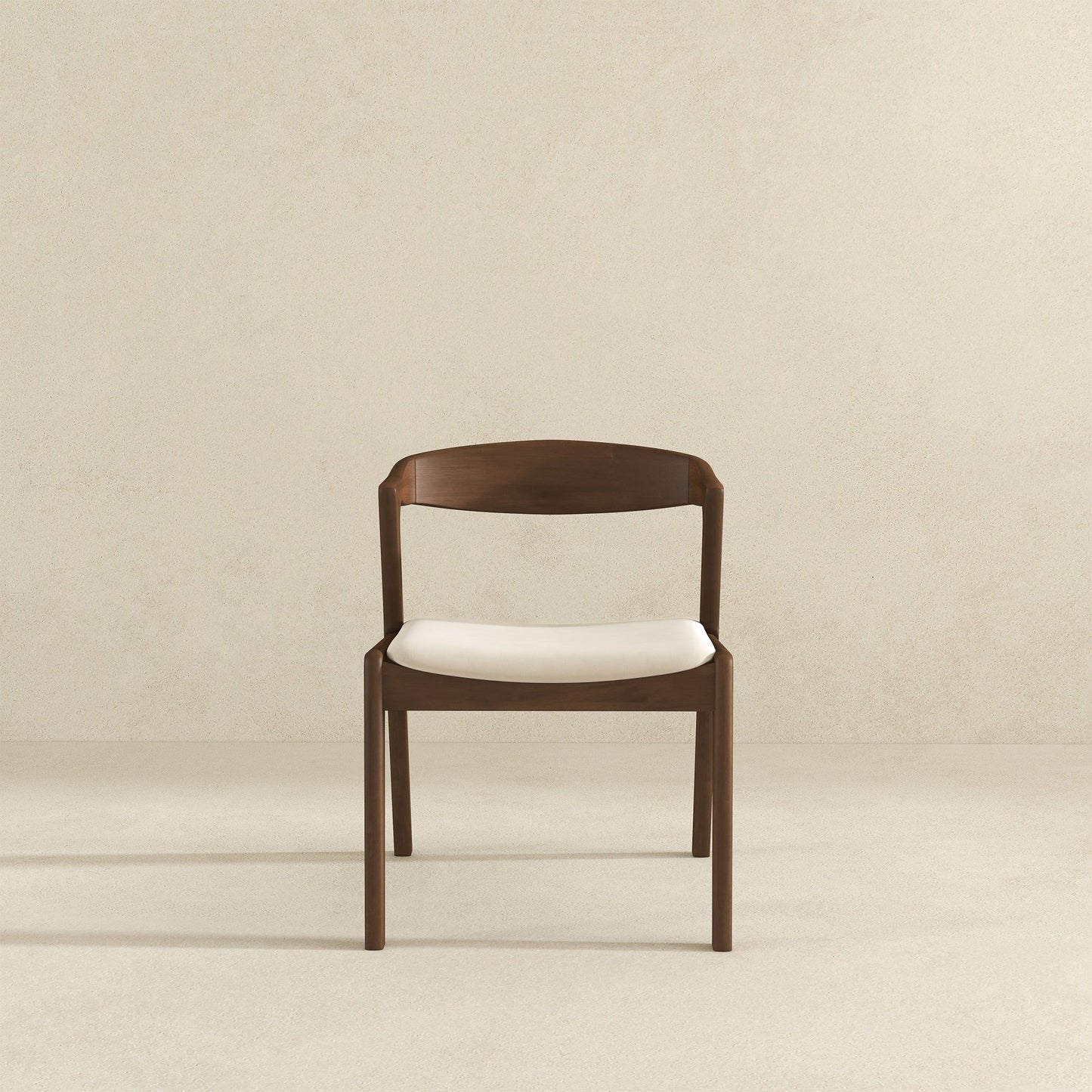 A set of Dakota Mid-Century Modern Velvet Dining Chairs, featuring curved backrests and white cushioned seats, is centered against a plain light beige wall and floor background.