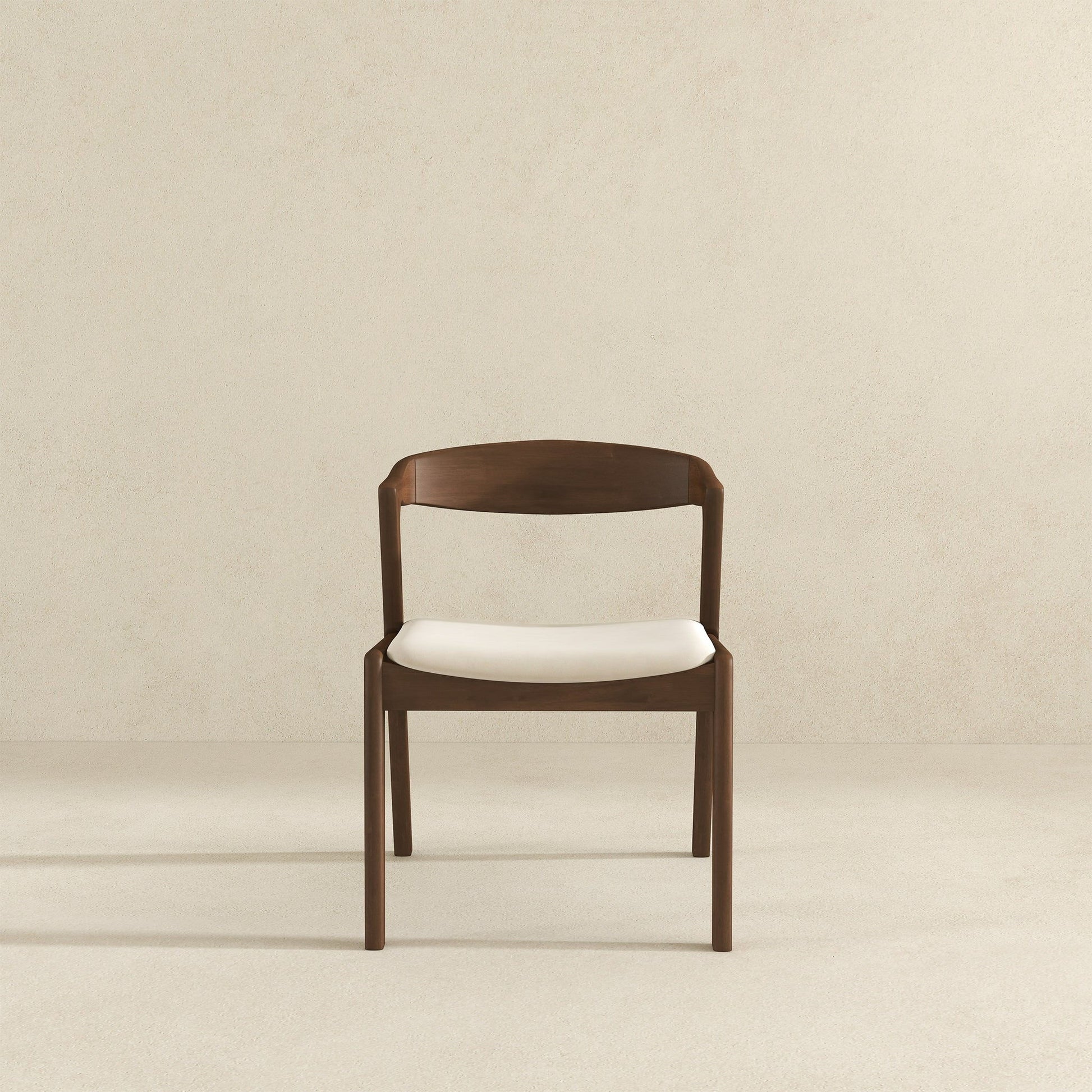 A set of Dakota Mid-Century Modern Velvet Dining Chairs, featuring curved backrests and white cushioned seats, is centered against a plain light beige wall and floor background.