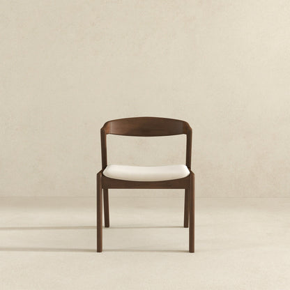 A set of Dakota Mid-Century Modern Velvet Dining Chairs, featuring curved backrests and white cushioned seats, is centered against a plain light beige wall and floor background.