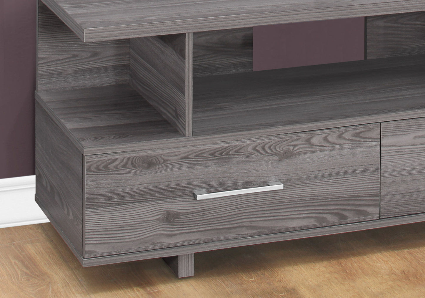 A close-up of the gray TV Stand, Console, Media Entertainment Center with a visible drawer and sleek silver handle, placed on a wood floor beside a purple wall and white baseboard.