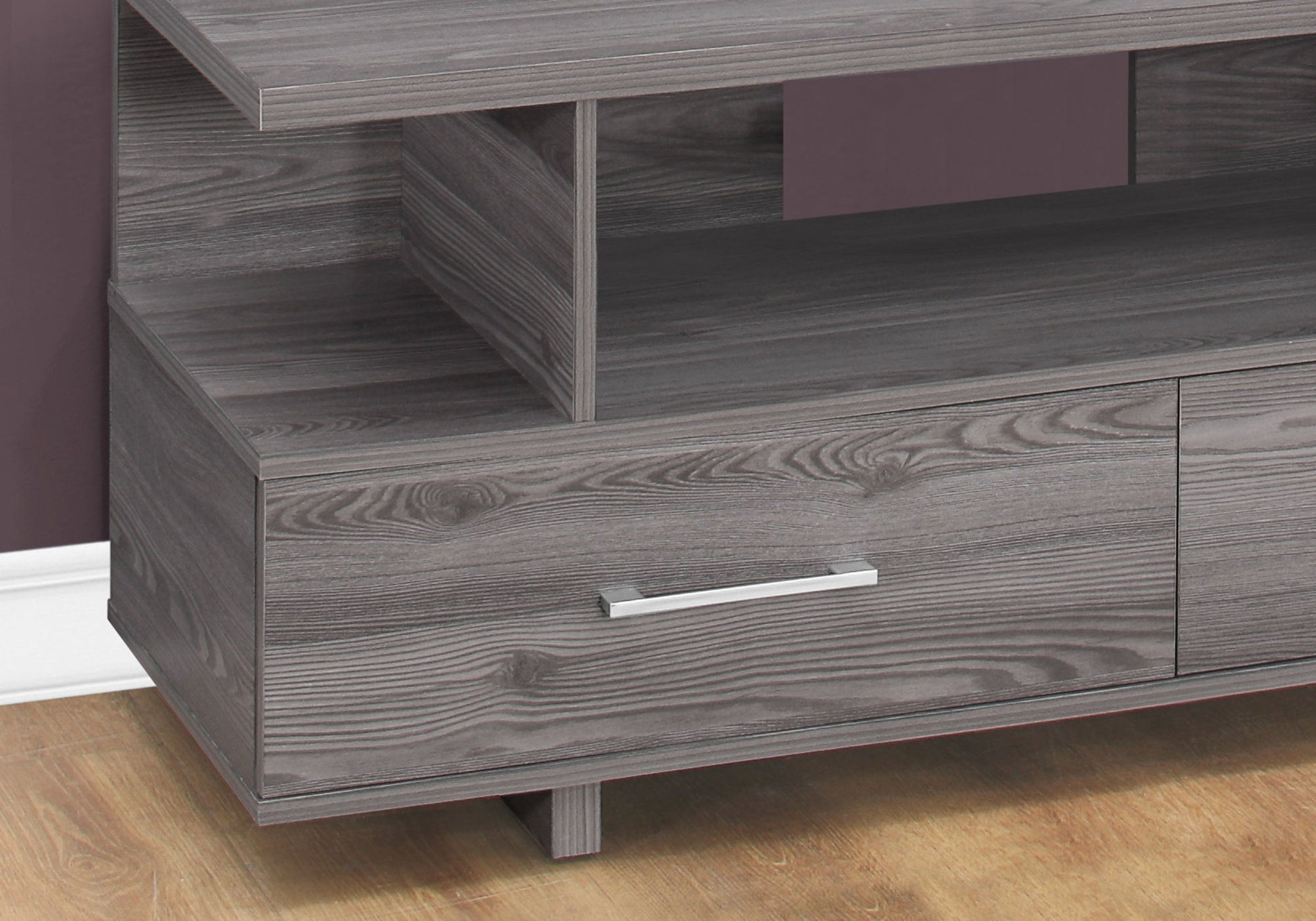 A close-up of the gray TV Stand, Console, Media Entertainment Center with a visible drawer and sleek silver handle, placed on a wood floor beside a purple wall and white baseboard.