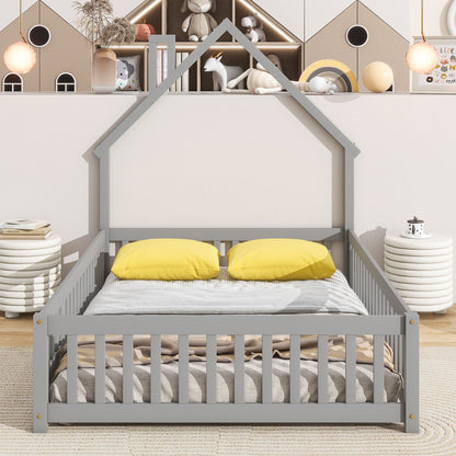 The House-Shaped Headboard Floor Bed With Fence features a gray frame, two yellow pillows, and a beige blanket in a cozy room with soft lighting, round side tables, and wall shelves decorated with toys and books behind it.