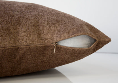 A close-up of a modern, brown decorative throw pillow with a partially open zipper exposing the hypoallergenic white insert. The square pillow sits on a smooth, reflective surface. Insert included.