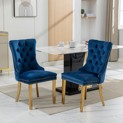 Two Nikki modern velvet dining chairs with tufted backs, gold-plated legs, and nailhead trim (set of 2) are on a beige rug in a bright dining room featuring a marble table and minimal decor.