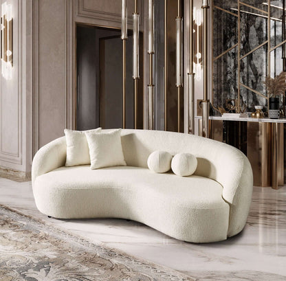 The Drake - Japandi Style Curvy Boucle Sofa in cream features two square and two round pillows, set in a luxurious room with marble floors, a decorative rug, golden chandeliers, and a mirrored accent wall.