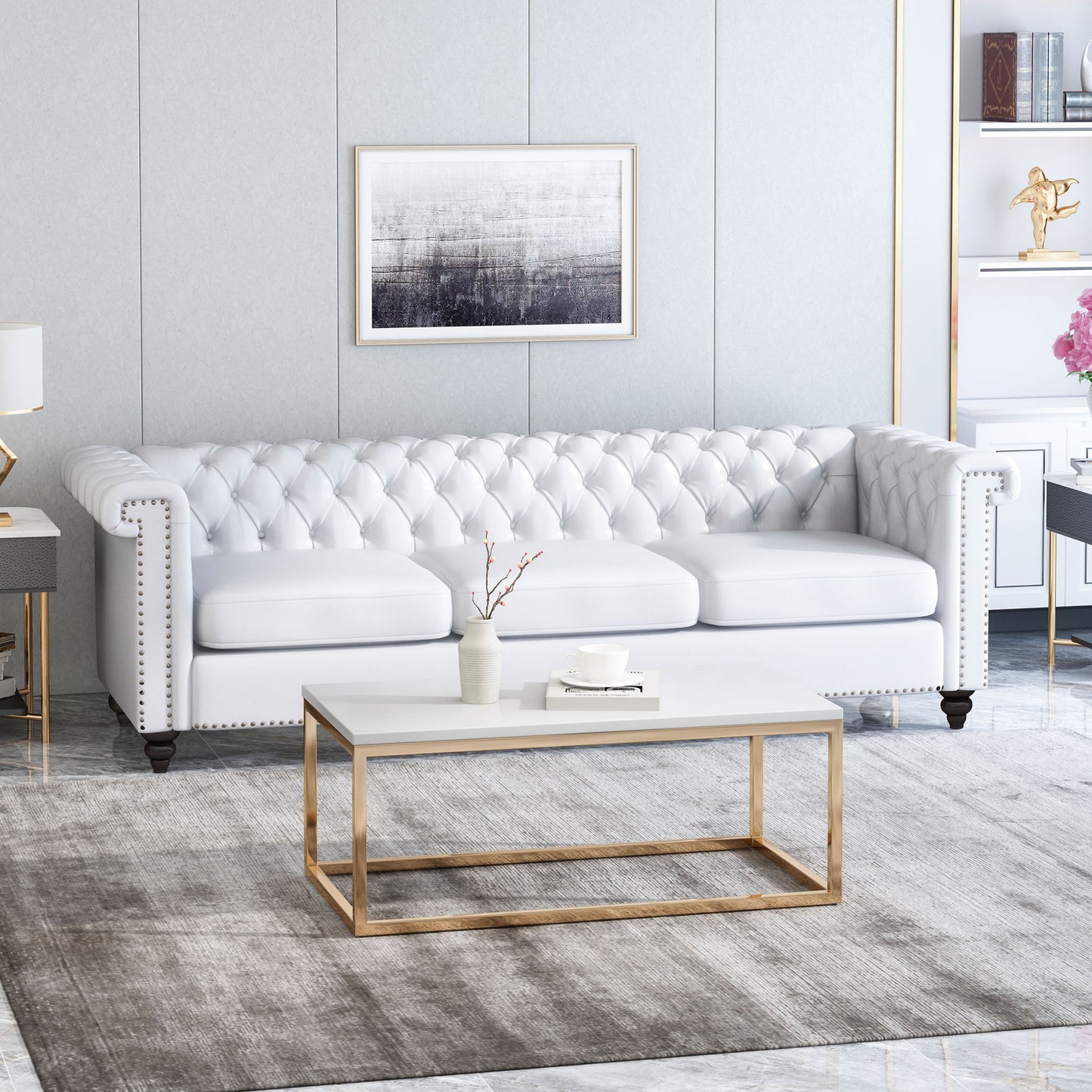 A modern living room featuring a Chesterfield Style 3 Seater Sofa with deep button tufting, a gold-framed rectangular coffee table, gray area rug, minimalist decor, and framed abstract artwork on a light-colored wall.