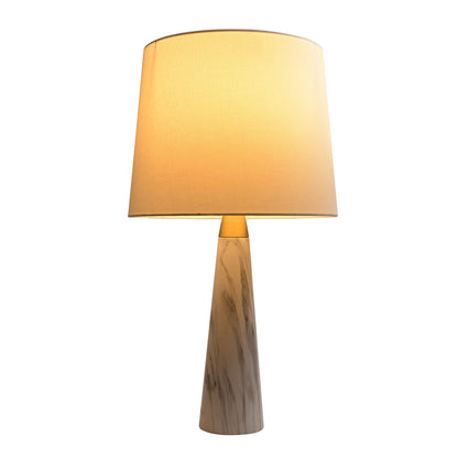 The Enclave Hydro Table Lamp features a gold finish, white cylindrical shade, and faux white marble conical base. The lamp is switched on and emits a warm, inviting glow.