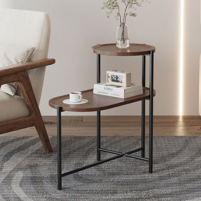 The Round Coffee Table With Storage Tray 2 Tier Oval End Tables Wooden Small Side Table for Living Room, featuring black metal legs, holds a digital clock, book, and vase with flowers beside an upholstered chair on a gray patterned rug.