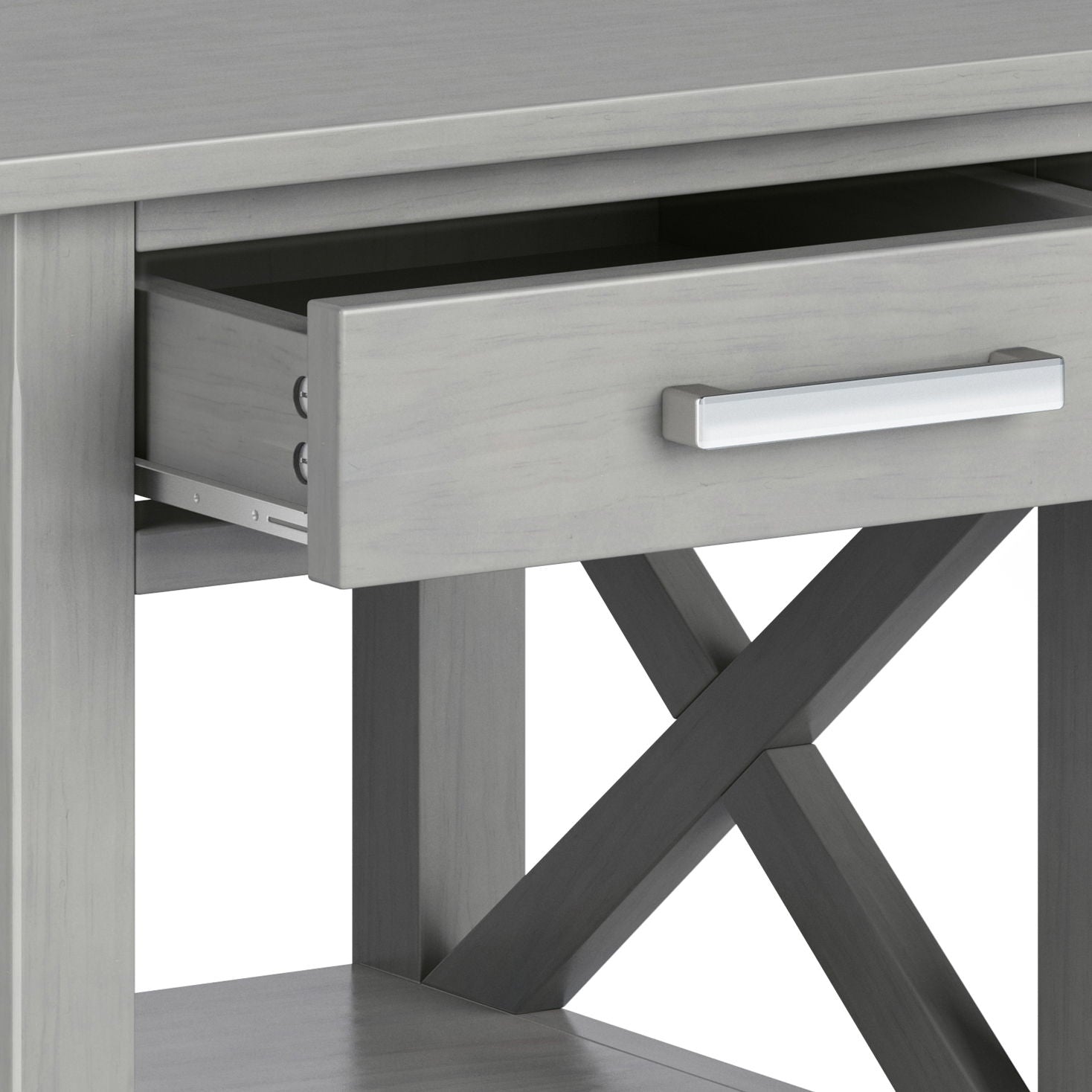 A close-up of the Kitchener - Handcrafted Table in gray shows an open drawer with a silver handle, crossed supports beneath, and a lower shelf.