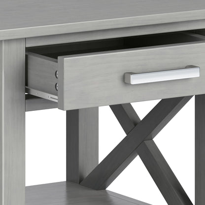 A close-up of the Kitchener - Handcrafted Table in gray shows an open drawer with a silver handle, crossed supports beneath, and a lower shelf.