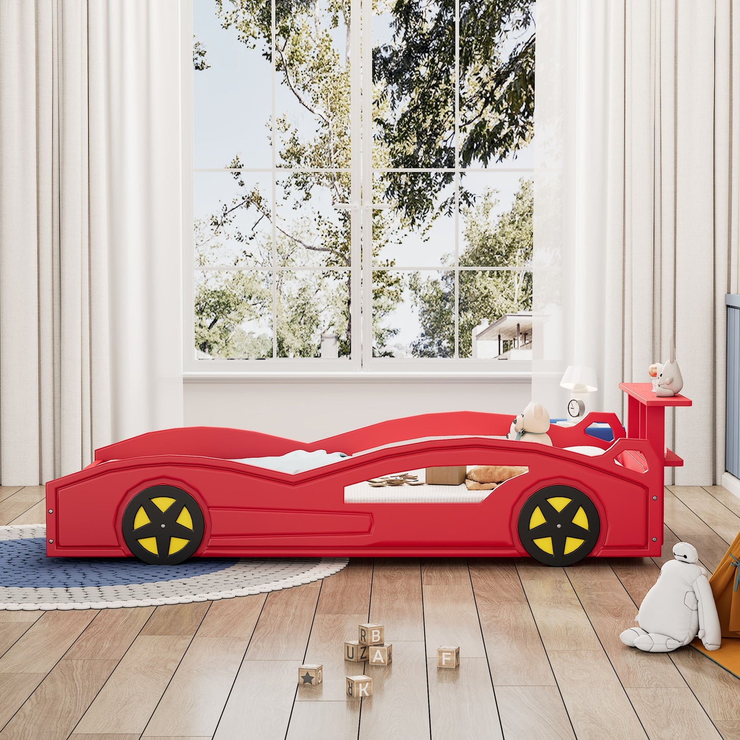 A child’s bedroom featuring the Wooden Race Car Bed, Car Shaped Platform Twin Bed With Wheels For Teens, surrounded by toys and stuffed animals, wooden alphabet blocks on a round rug, and large windows with white curtains showing trees.