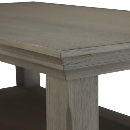 A close-up of the Acadian - Narrow Side Table, Handcrafted, highlights its grey-finished wooden tabletop, legs, and part of the lower shelf with a smooth, slightly weathered texture.
