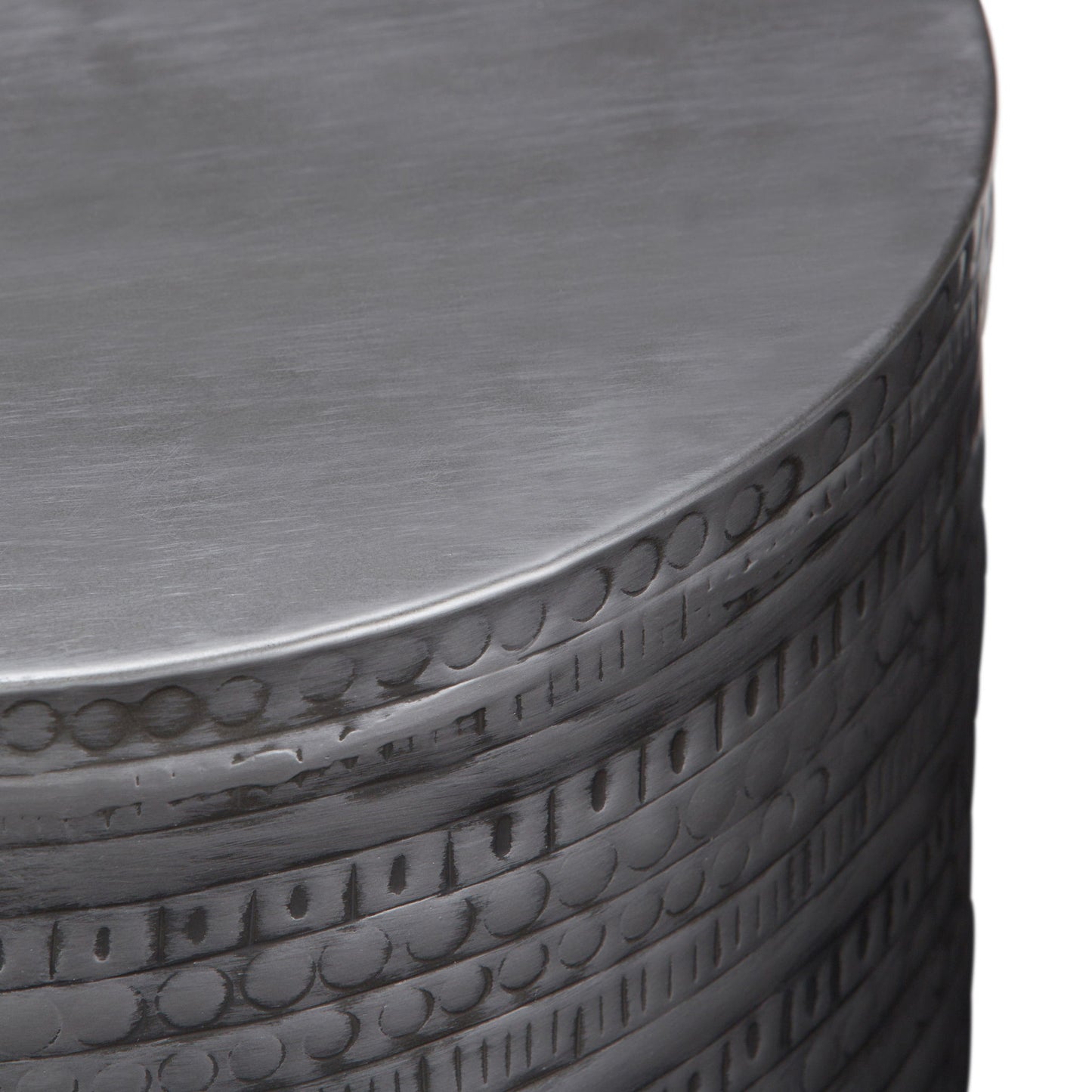 A close-up of the Johnsen - Handcrafted Large Metal Accent Table reveals engraved circular and linear patterns along the side, highlighted by its brushed silver finish.