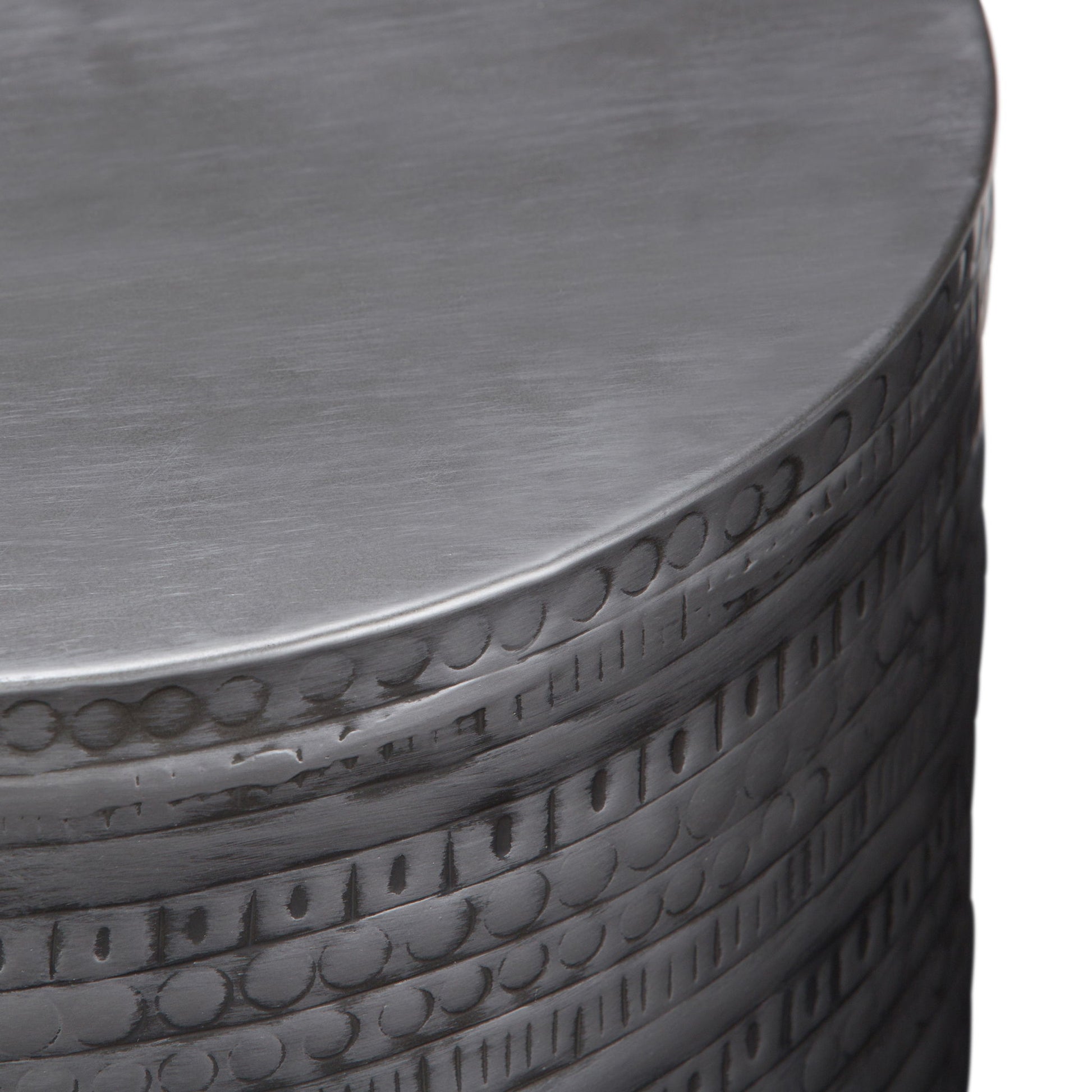 A close-up of the Johnsen - Handcrafted Large Metal Accent Table reveals engraved circular and linear patterns along the side, highlighted by its brushed silver finish.