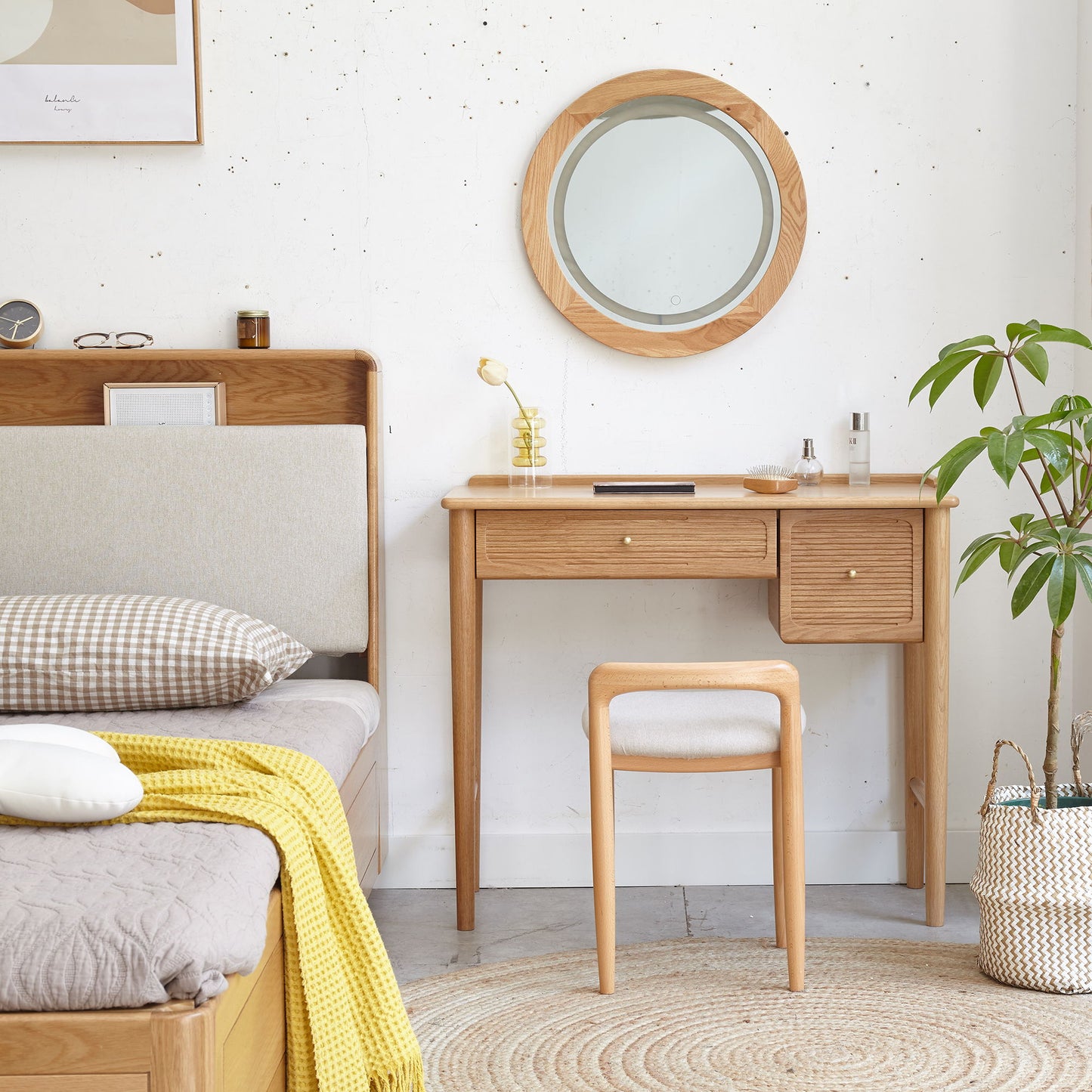 A cozy bedroom showcases the Stool Bed For Dining Room - Natural, complemented by a matching vanity with round mirror, cushioned stool, potted plant, woven basket, and soft decor in neutral tones.