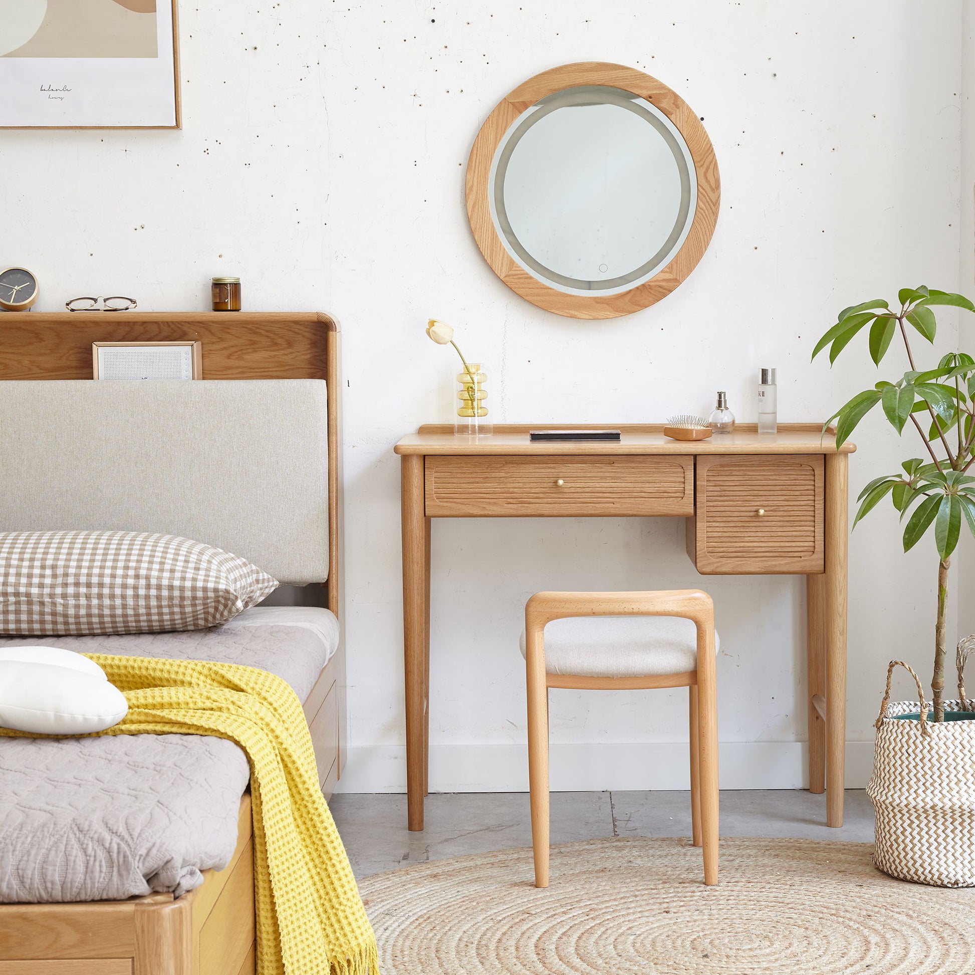 A cozy bedroom showcases the Stool Bed For Dining Room - Natural, complemented by a matching vanity with round mirror, cushioned stool, potted plant, woven basket, and soft decor in neutral tones.