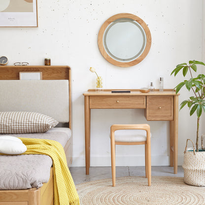A cozy bedroom showcases the Stool Bed For Dining Room - Natural, complemented by a matching vanity with round mirror, cushioned stool, potted plant, woven basket, and soft decor in neutral tones.