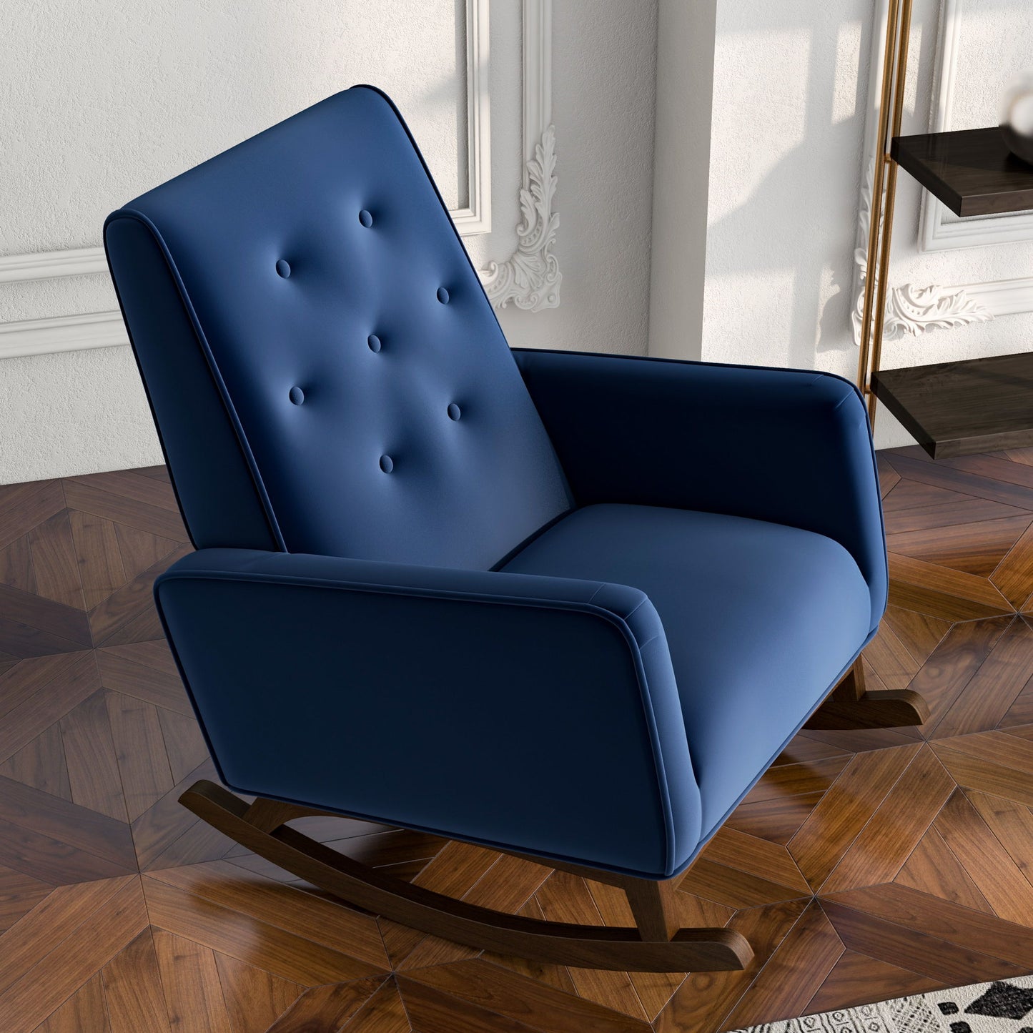 The Demetrius Solid Wood Rocking Chair, featuring modern blue upholstery and a button-tufted backrest, stands on a patterned wooden floor in a stylish room with white paneled walls and decorative molding.