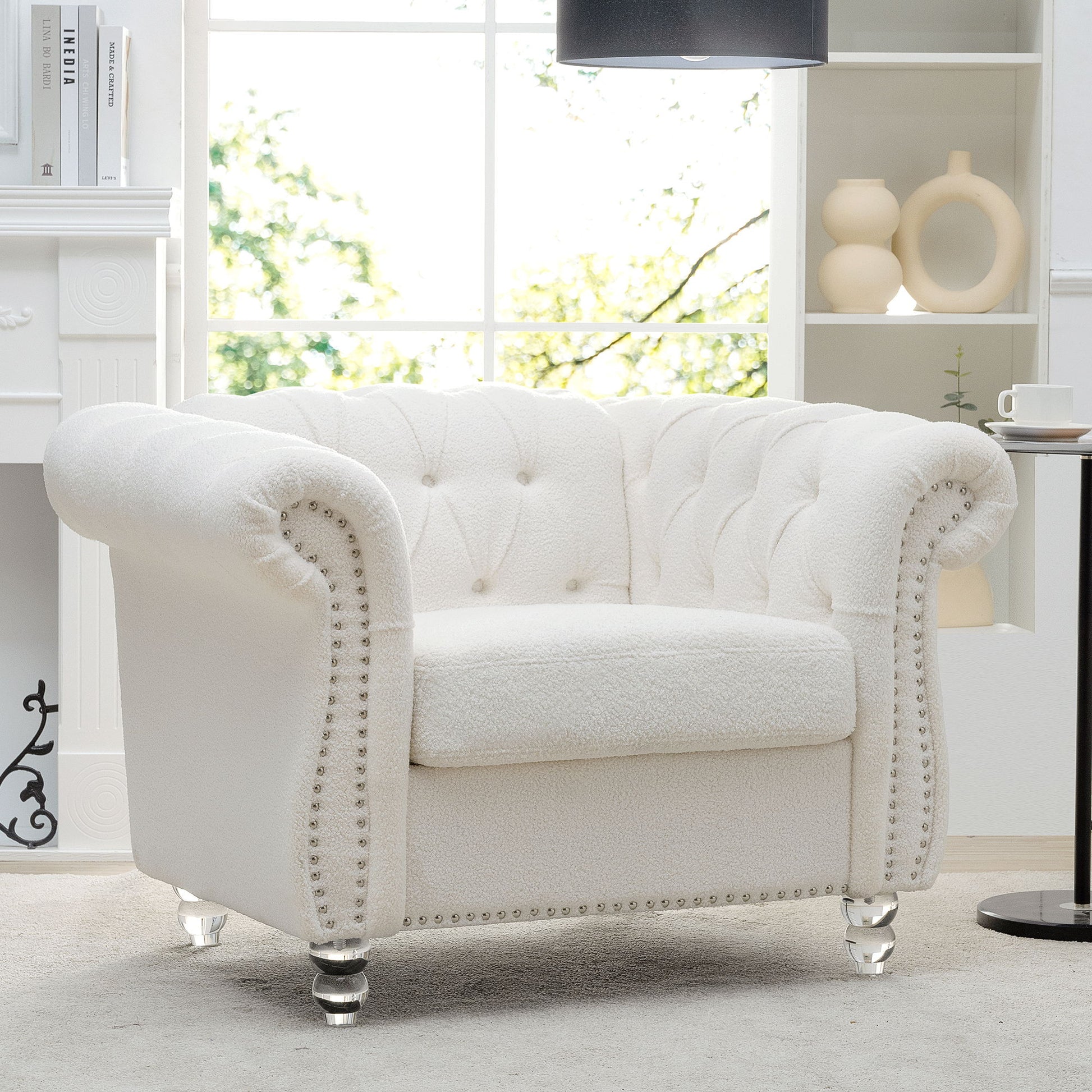 A 1 Seater Sofa For Living Room with white tufted upholstery, rolled arms, and silver nailhead trim sits by a window in a bright room with shelves and a fireplace in the background.