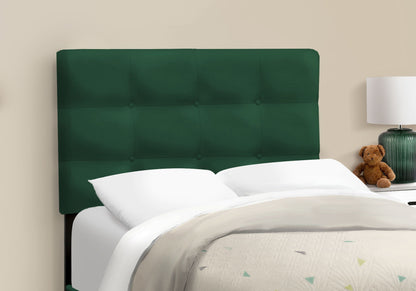 A Bed, Upholstered, Frame Only, Transitional with a dark green tufted headboard is set against a beige wall, featuring white bedding and pillows. A nightstand with a lamp and brown teddy bear stands beside it.