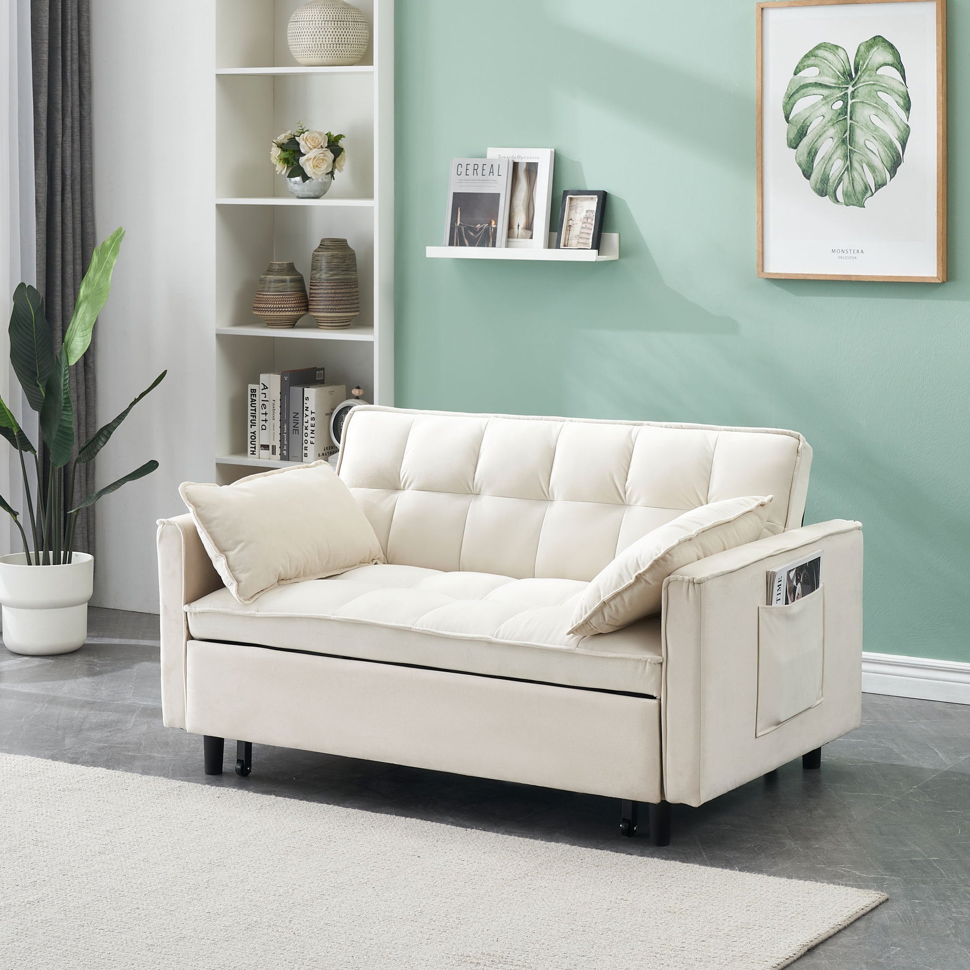 The Modern Velvet Sofa 3-in-1 Convertible Sleep Sofa Bed with tufted cushions, pillows, and pockets is showcased in a stylish living room with a green wall, framed leaf print, potted plant, decorative shelves, and a light rug on a gray floor.