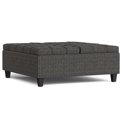 The Harrison Upholstered Coffee Table Storage Ottoman features a large square design, dark wooden legs, and a tufted top in textured dark gray fabric.