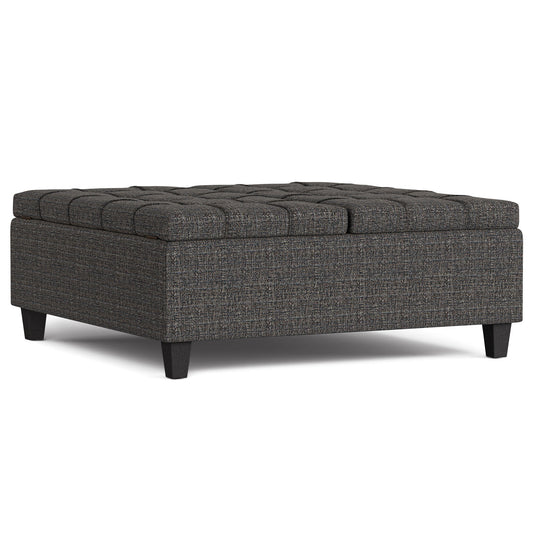 The Harrison Upholstered Coffee Table Storage Ottoman features a large square design, dark wooden legs, and a tufted top in textured dark gray fabric.