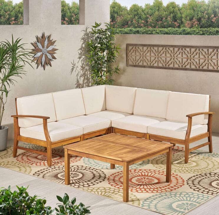 The Perla - 6 Pieces Sofa Set with white cushions sits on a colorful rug next to its matching coffee table on a patio, surrounded by plants and decorative wall art.