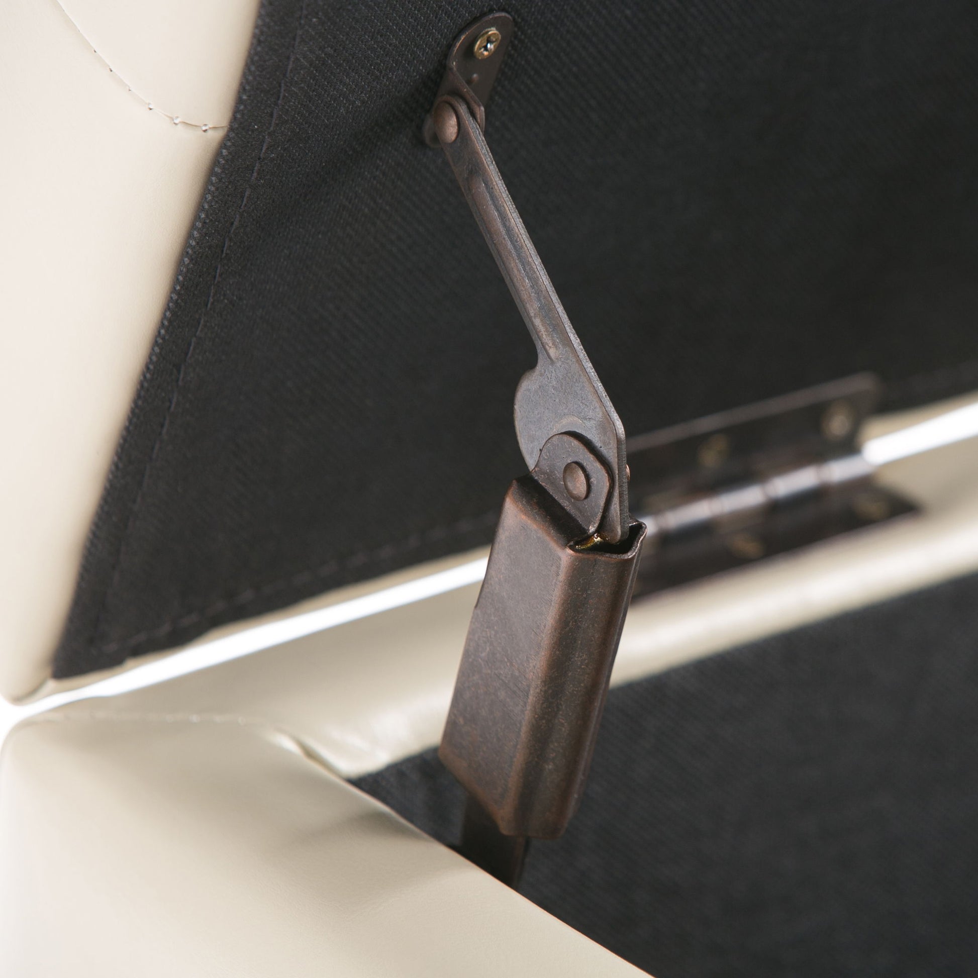 Close-up of the metal hinge and support bracket inside the Cosmopolitan Upholstered Storage Ottoman, showing its padded light-colored exterior and black interior fabric lining.