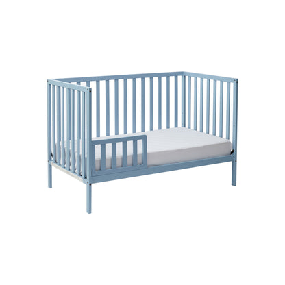 The Palmer 3-in-1 Convertible Island Crib is shown in light blue with vertical slats, an open front side, and a white mattress, set against a plain white background.