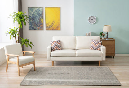 A modern living room with the Bahamas Sofa Set featuring 2 throw pillows, an armchair, a wooden sideboard with a lamp, two abstract paintings, a wall clock, a potted plant, and a light gray patterned rug.
