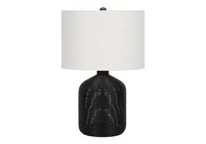 A modern table lamp with a rattan-textured, rounded black base and a large cylindrical white shade, shown against a plain white background.