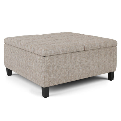 The Harrison Upholstered Coffee Table Storage Ottoman features a square beige design with tufted detailing on top and short black legs, shown on a white background.