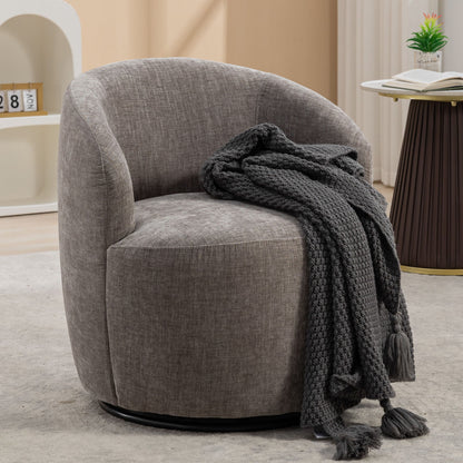 A Chenille Fabric Swivel Accent Armchair Barrel Chair with a curved backrest sits on a light rug. A chunky dark gray knit throw is draped over the arm, next to a small round table with a book and plant.
