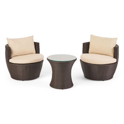 The Kono - Chat Set Outdoor Furniture includes two round wicker chairs with beige cushions and matching back pillows, placed on each side of a small round wicker table with a glass top.