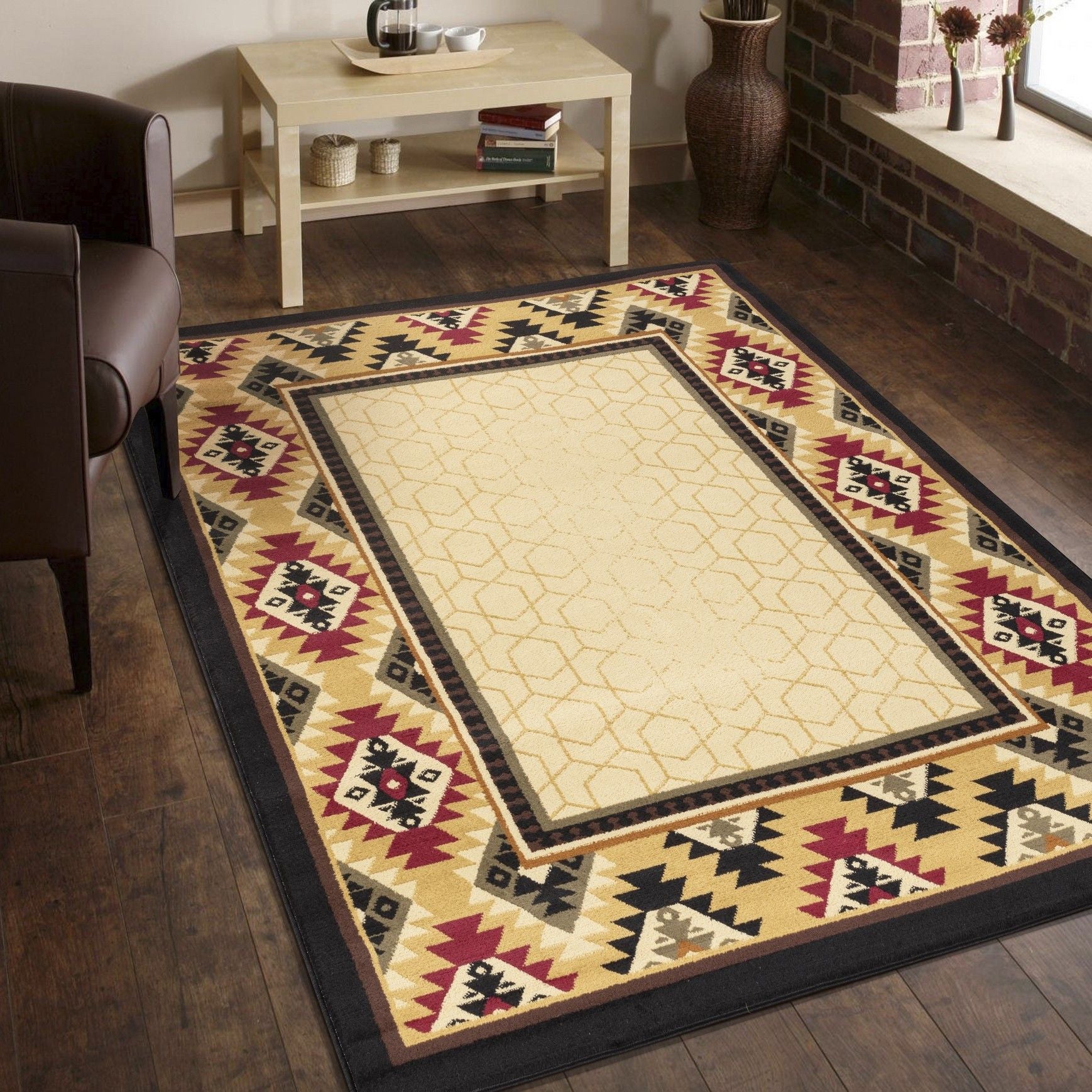 A living room with the Tribes - GC_YLS4007 Southwest Area Rug, a beige geometric rug with a red, black, and gold patterned border, plus a brown armchair, light wood table, brick walls, large window, and potted plants.