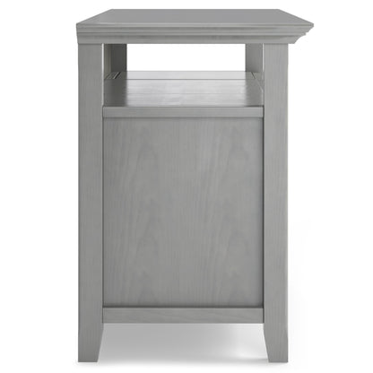 A side view of the Amherst - TV Media Stand, Handcrafted, in gray wood with straight legs, a lower shelf, and solid side panel. Features a simple, modern design.