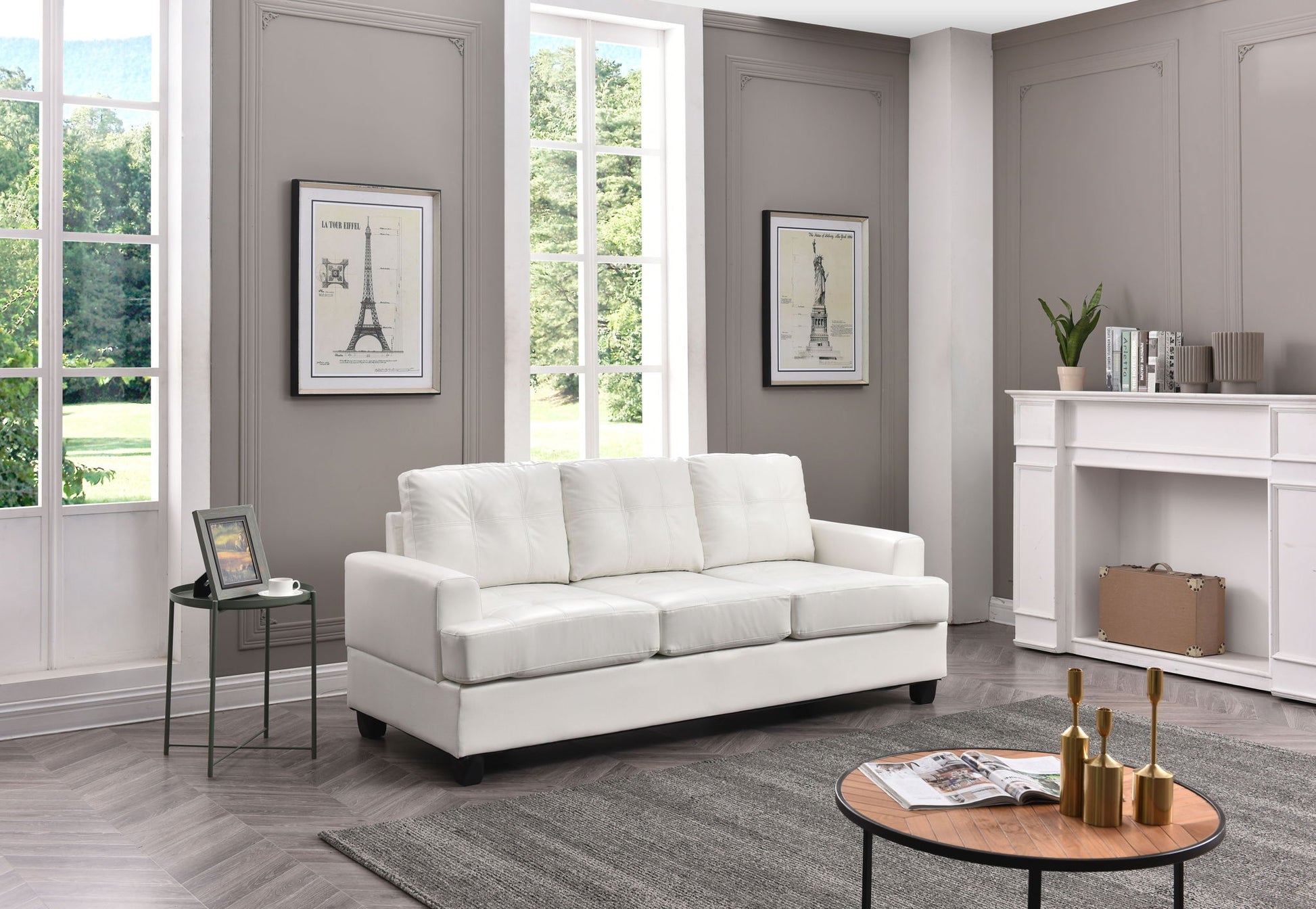 A modern living room featuring the Sandridge - Sofa, a round wooden coffee table, framed art on gray walls, large windows with greenery outside, a small side table with photo frame and plant, neutral rug, and fireplace.