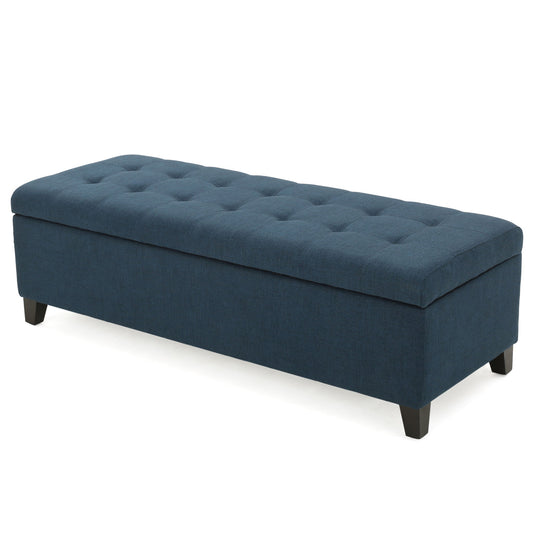 The Nebulous Ottoman is a navy blue fabric upholstered storage bench with a diamond tufted seat and short black wooden legs, shown against a white background.
