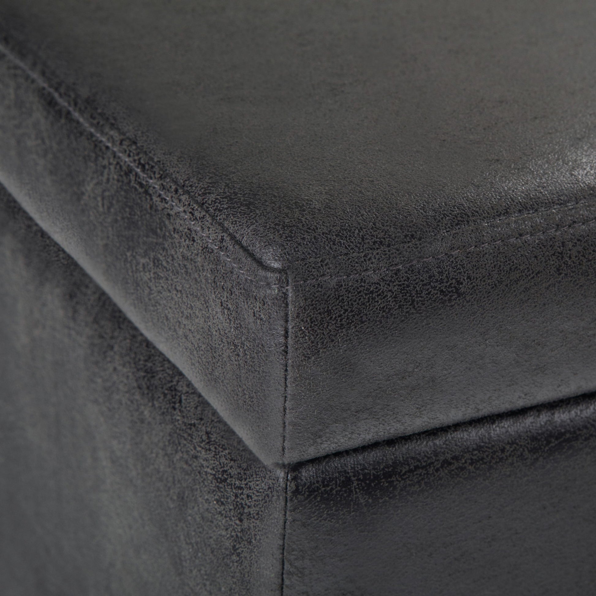 Close-up of the Avalon Storage Ottoman Bench in Distressed Black, highlighting its textured faux leather upholstery, detailed stitching, and material grain.