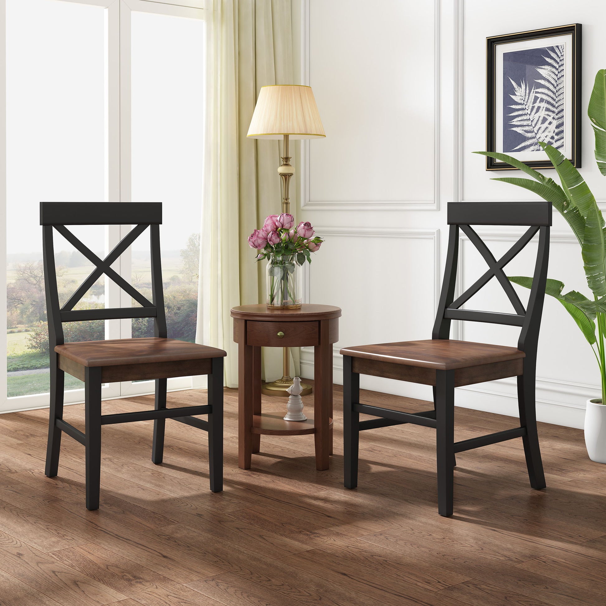 Two Plethora Dining Chairs with X-shaped backs and dark frames sit by a small round side table topped with a lamp and vase. Large windows, light curtains, framed art, and a tall plant add to the cozy atmosphere.