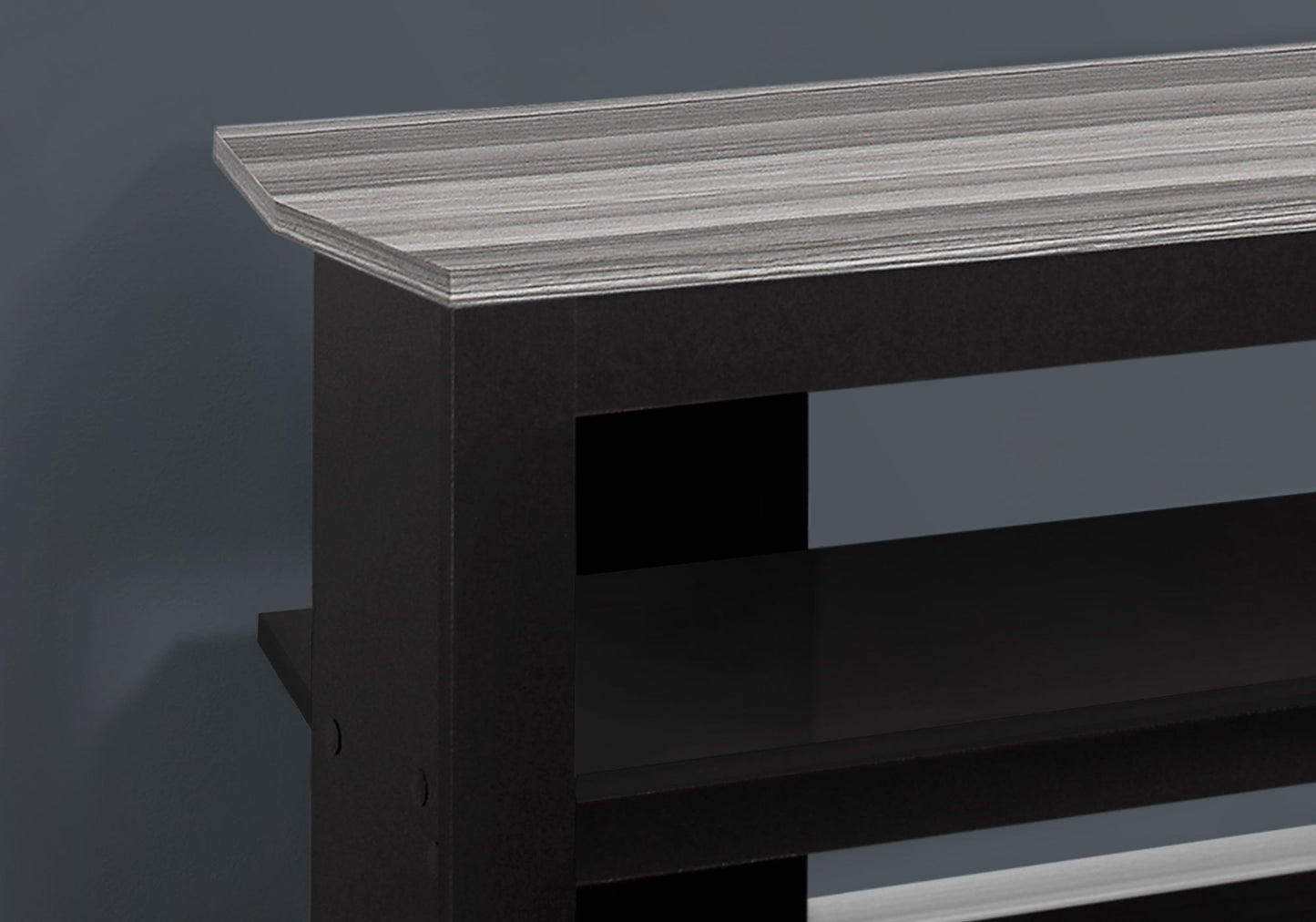A close-up of the TV Stand Console Media Entertainment Center, featuring a black frame with a gray wood-grain top and 3 storage shelves, set against a matte dark gray wall.