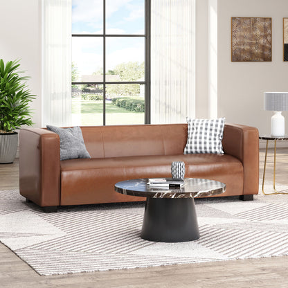A modern living room featuring the Contemporary 3 Seater Sofa With Tuxedo Design in brown leather, two patterned pillows, a round black and marble coffee table, sheer-curtained window, a green plant, and wall art on a beige wall.