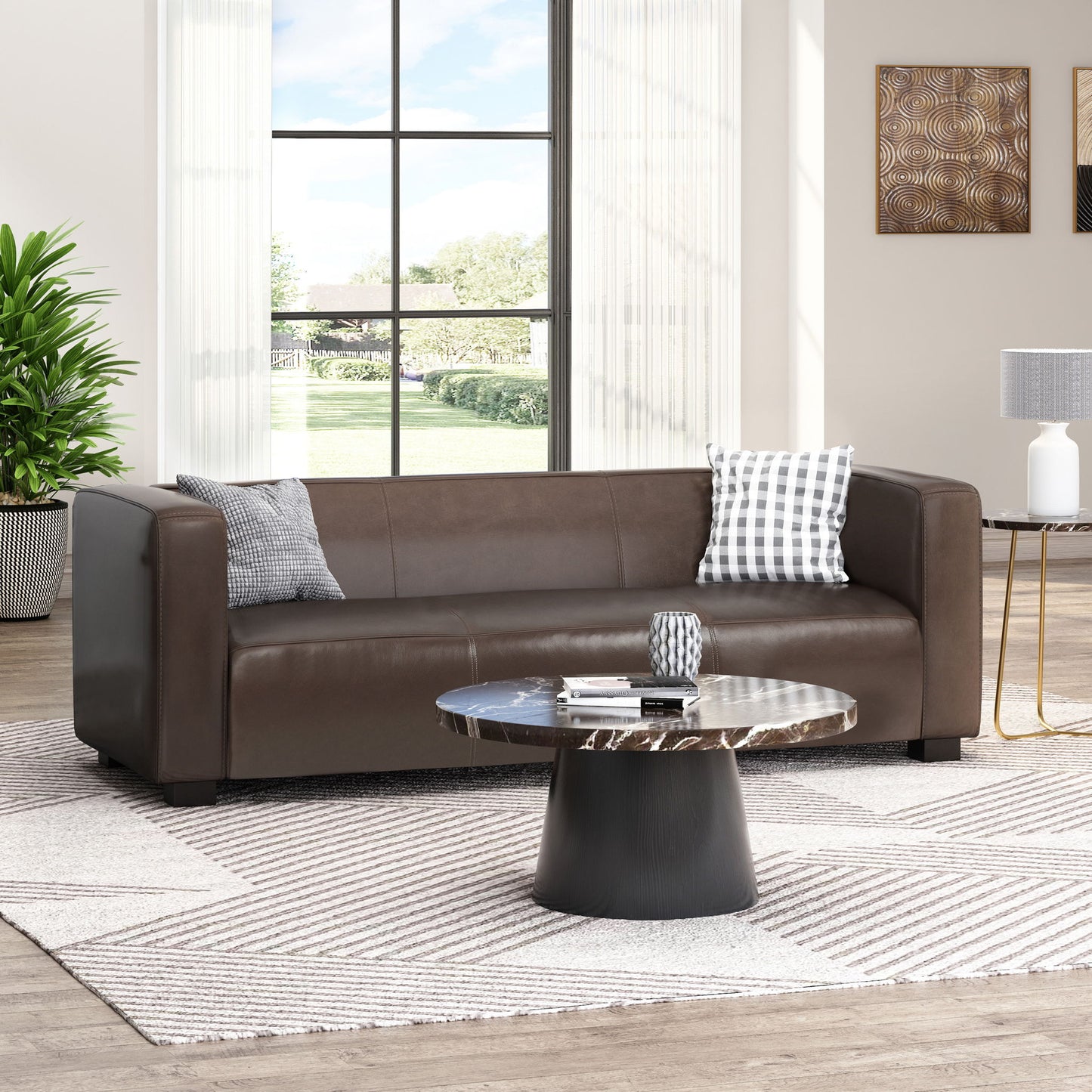 A modern living room with a Contemporary 3 Seater Sofa With Tuxedo Design in brown leather, two patterned throw pillows, a round black coffee table, geometric rug, potted plant, and large windows allowing natural light in.