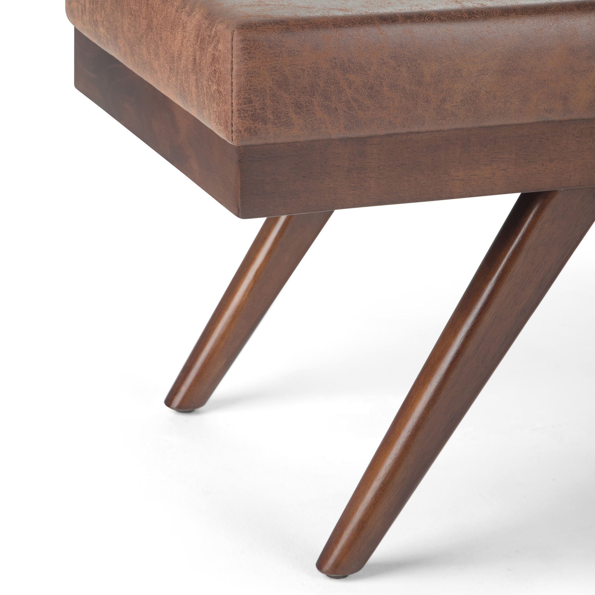 Close-up of the Chanelle Mid-Century Ottoman Bench featuring angled wooden legs and a brown leather-upholstered seat, set against a white background.